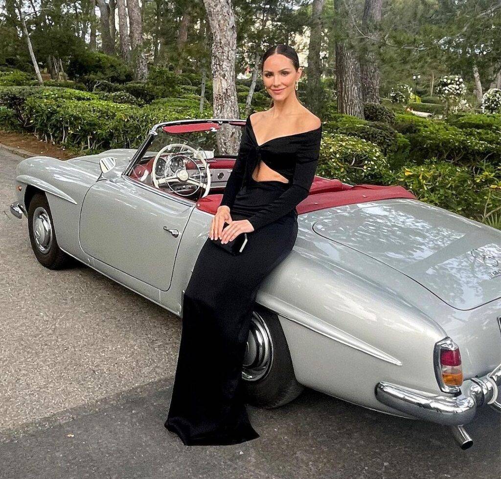 Katherine in the black sexy dress while sitting on the car and poses for a picture 