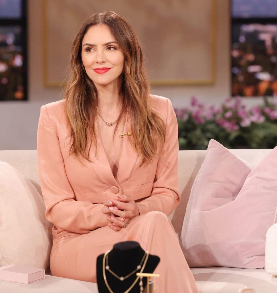 katharine mcphee foster in the peach stunning outfit while sitting on the sofa and poses for a photo