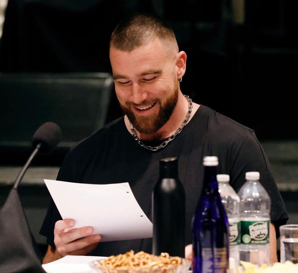 Travis Kelce in the black t-shirt pair with chunky necklace while reading a script