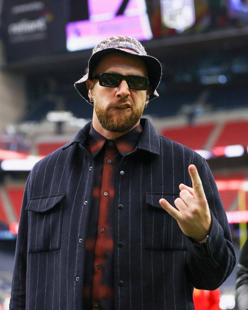 Travis Kelce in the maroon and black dress shirt pair with bucket hat while poses for a photo