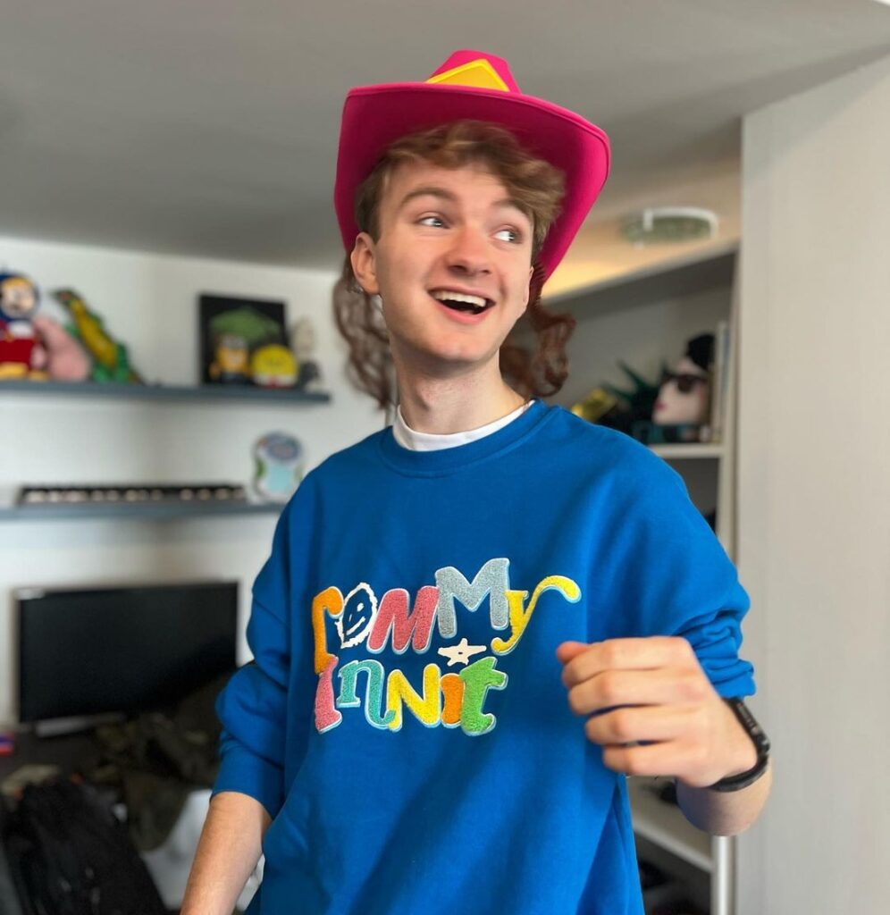 TommyInnit in the blue t-shirt pair red hat while poses for a picture