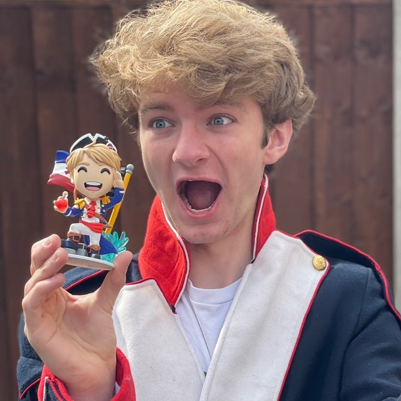 TommyInnit in the blue and red jacket while holding a toy in his hand and poses for a photo