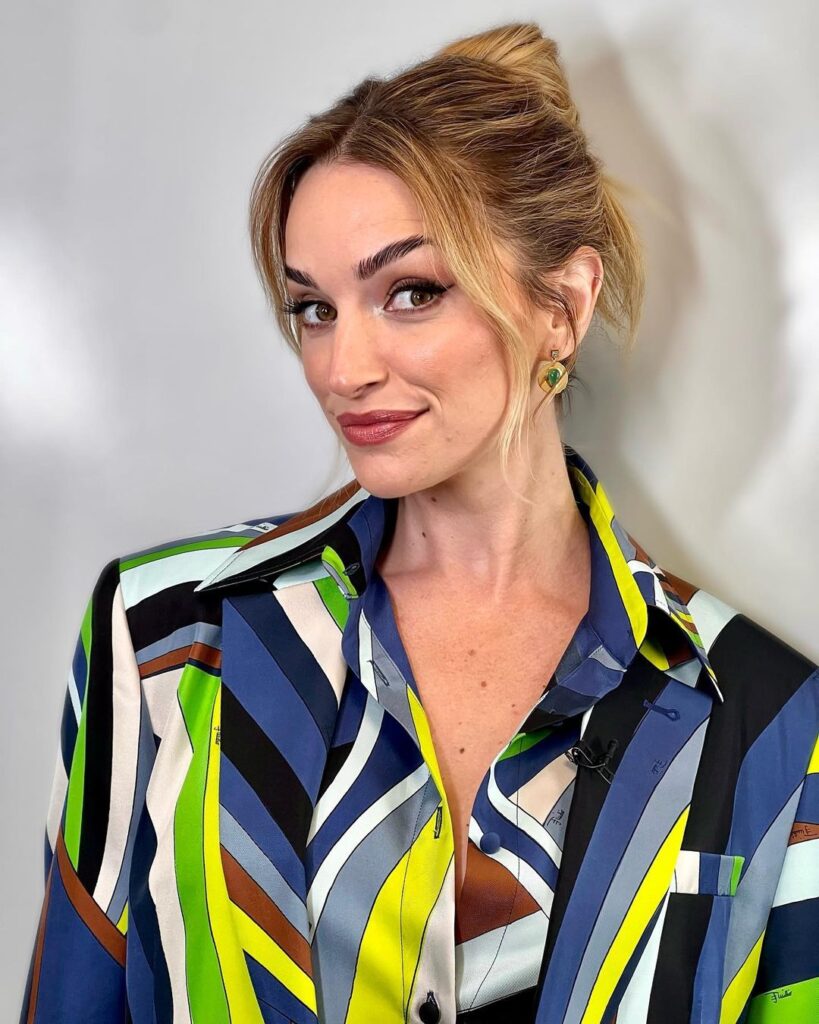 Brianne Howey in the multi-colors shirt and studs while smiling towards camera for taking a picture