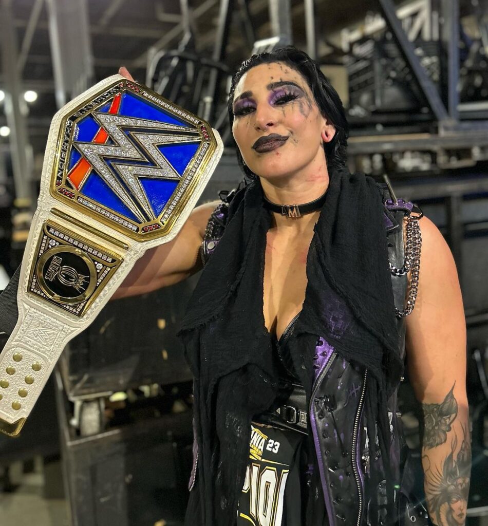 Rhea Ripley in the black wrestling costume while smiling towards camera and poses for a photo