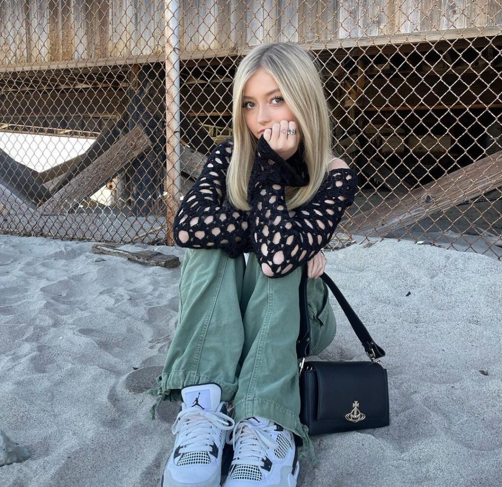 Emily Dobson in the black wool shirt piar with green pants and white joggers while poses for a photo