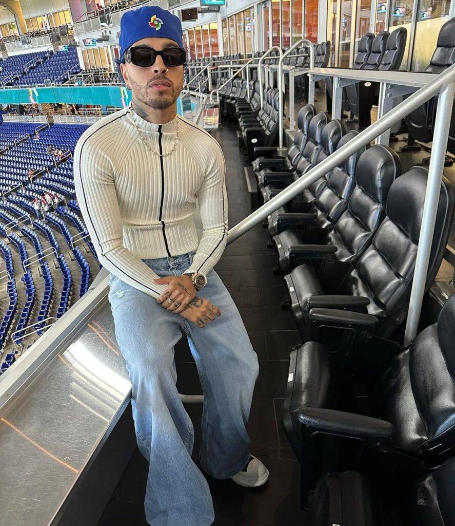 Rauw Alejandro in the front zip off-white shirt pair with denim jeans, black goggles and blue cap