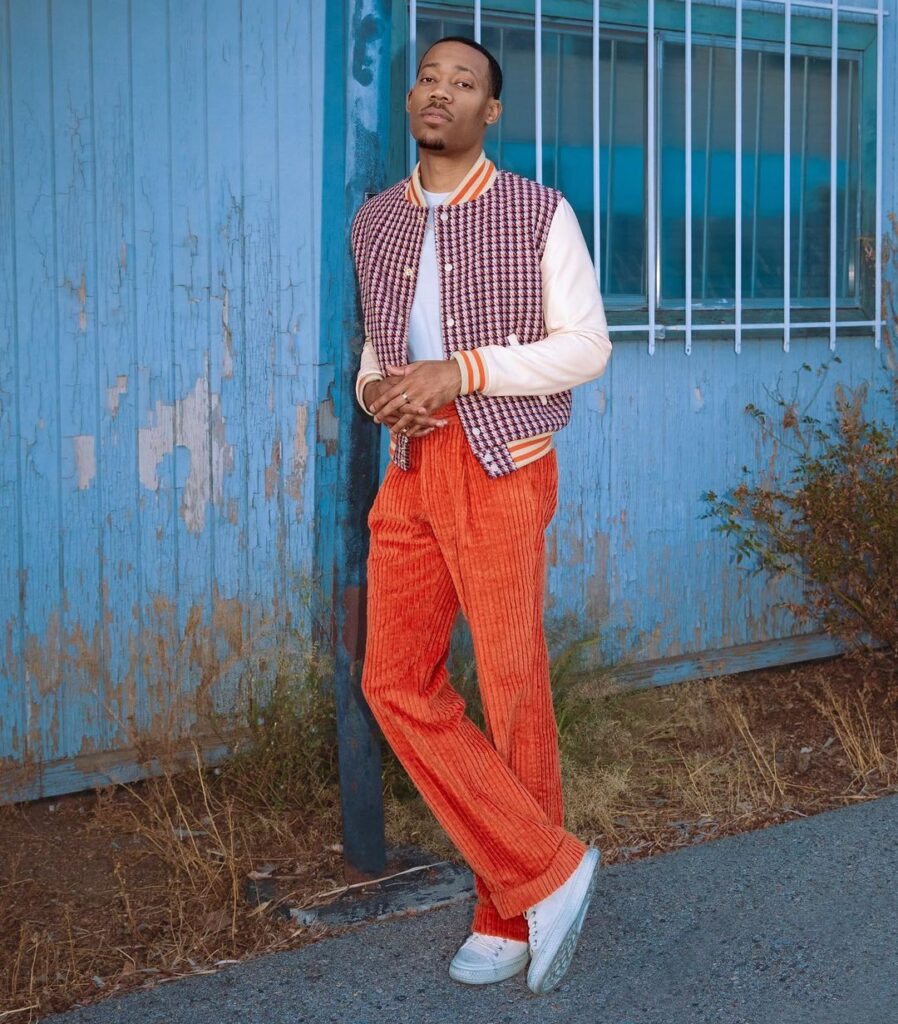 Tyler James Williams in the white shirt pair with a matching jacket and joggers while poses for a photo