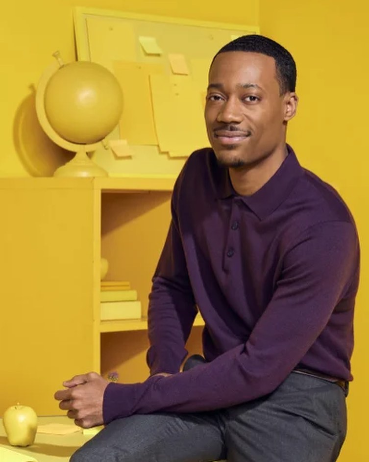 Tyler James Williams in the purple dress shirt paired with grey pants while smiling towards camera