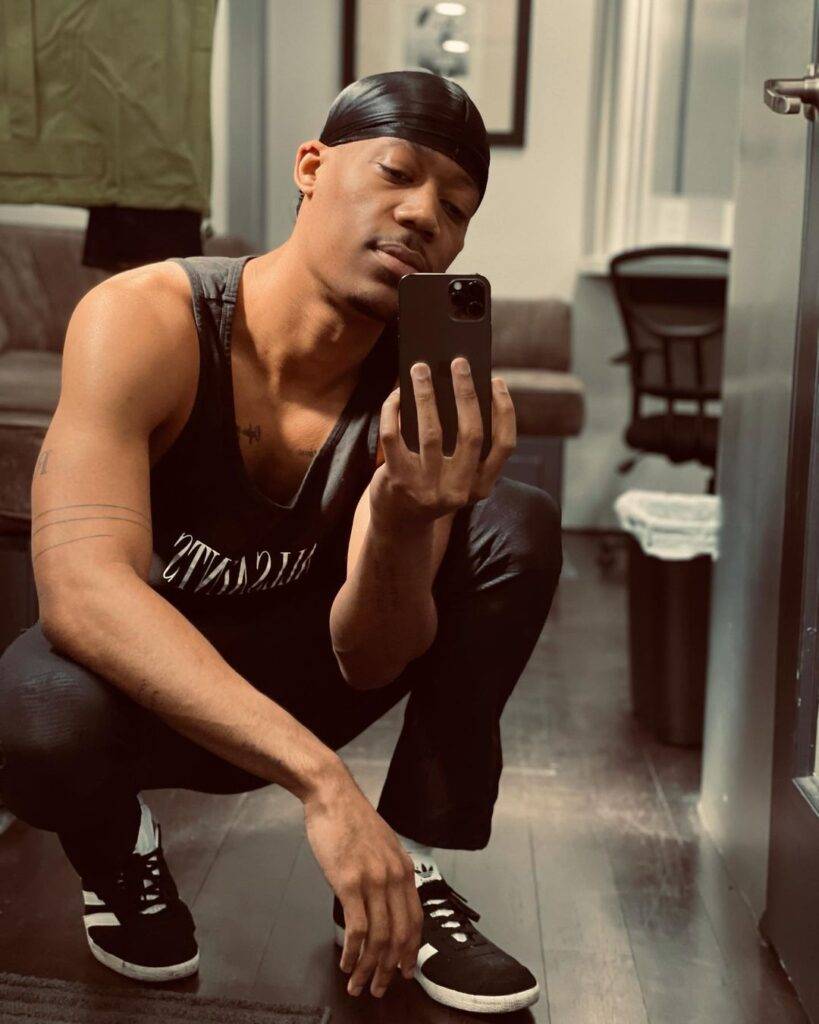 Tyler James Williams in the black sleeveless shirt pair with matching trouser while taking picture in the front of mirror