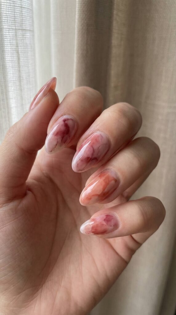 Watercolor wash nail art in pink and burgundy tones on almond-shaped nails