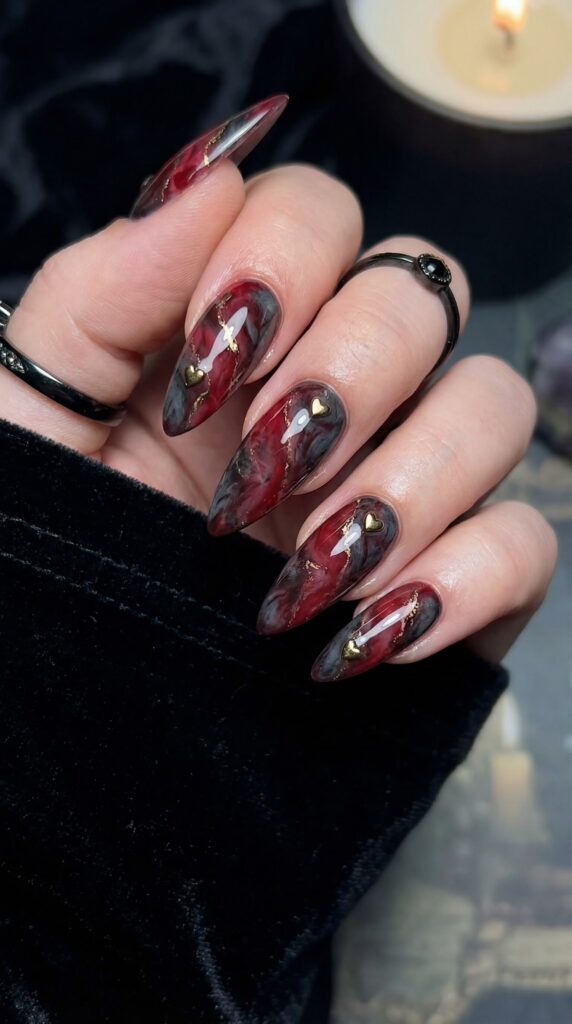 Gothic black and red marble nail art with gold heart charms on stiletto nails