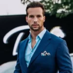 Tristan Tate in the blue dress shirt pair with blue coat while looking towards camera