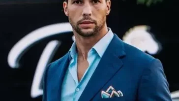 Tristan Tate in the blue dress shirt pair with blue coat while looking towards camera