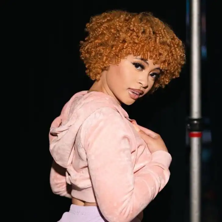 Ice Spice in the crop pink hoodie pair with purple shorts while looking towards camera