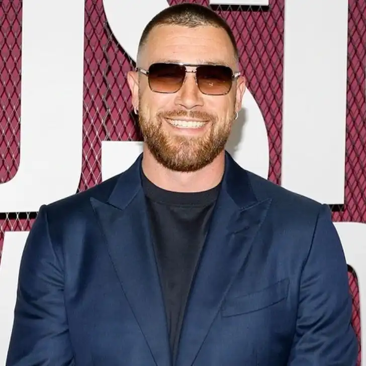Travis Kelce in the stunning blue outfit pair with a watch and goggles while smiling towards camera