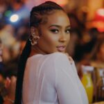 Kayla Nicole in the white crop top pair with elegant earnings while looking towards camera
