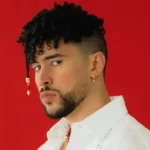 Bad bunny in the white shirt pair with elegant jewellery while looking towards camera