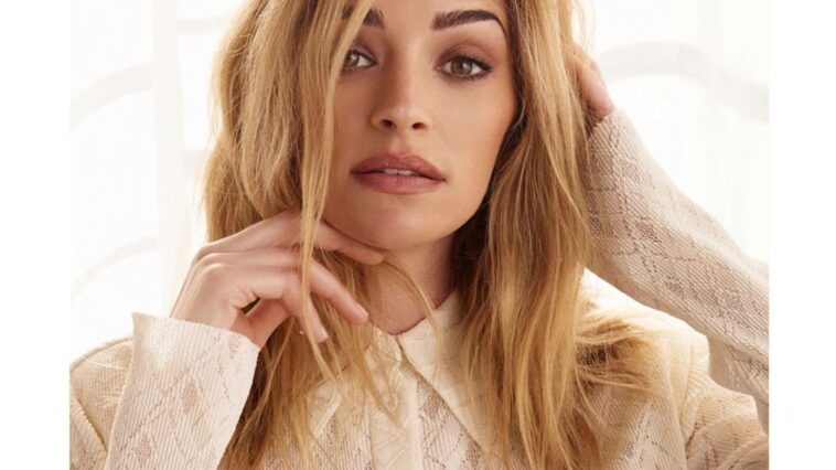Brianne Howey in the peach front button top paired with blue jeans while looking camera