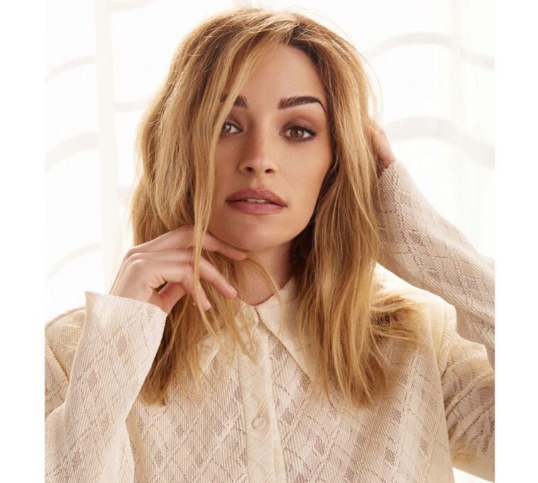 Brianne Howey in the peach front button top paired with blue jeans while looking camera