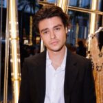 Felix Mallard in the white dress shirt pair with white coat and dress pant while poses for a photo