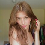 Jenny Roselie in the grey sexy top pair with drop earrings while looking towards camera
